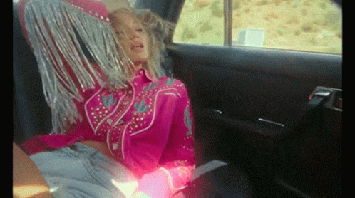 A Woman In A Pink Fringed Shirt Sits In The Back Seat Of A Car GIF