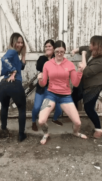 A Woman In A Pink Hoodie Has A Tattoo On Her Leg And Is Surrounded By Other Women GIF