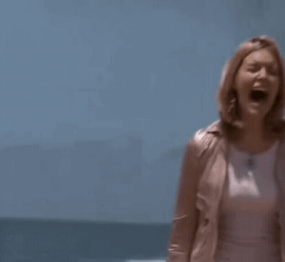 A Woman In A Pink Jacket And A White Skirt Is Standing On A Beach . GIF