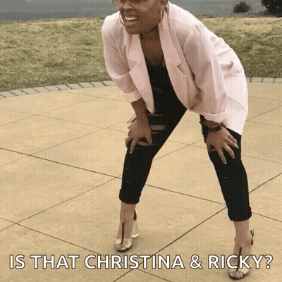 A Woman In A Pink Jacket And Black Pants Is Kneeling On A Sidewalk With The Caption Is That Christina & Ricky ? GIF