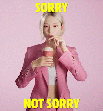 A Woman In A Pink Jacket Drinking From A Cup With The Words " Sorry Not Sorry " Written Above Her GIF