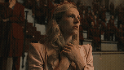 A Woman In A Pink Jacket Has Her Hands Folded In Front Of A Crowd GIF