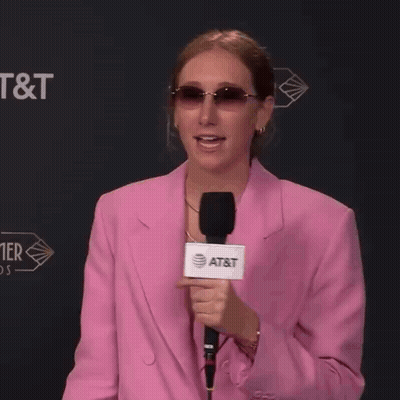 A Woman In A Pink Jacket Holds A Microphone That Says At & T On It GIF