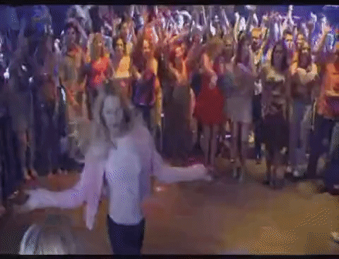 A Woman In A Pink Jacket Is Dancing In Front Of A Crowd Of People . GIF