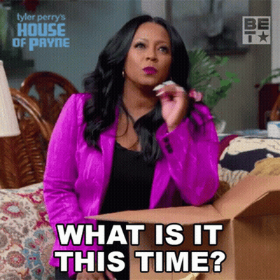 A Woman In A Pink Jacket Is Holding A Cardboard Box And Says What Is It This Time GIF