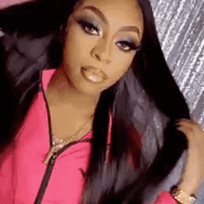 A Woman In A Pink Jacket Is Holding Her Hair In Her Hand . GIF