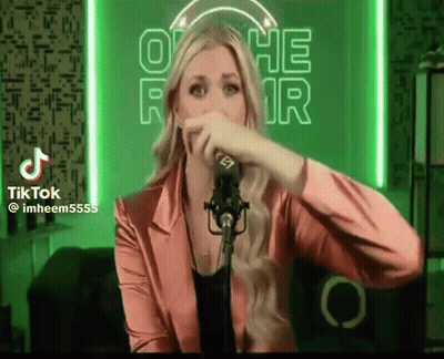 A Woman In A Pink Jacket Is Singing Into A Microphone In Front Of A Neon Sign That Says Othe Fair GIF