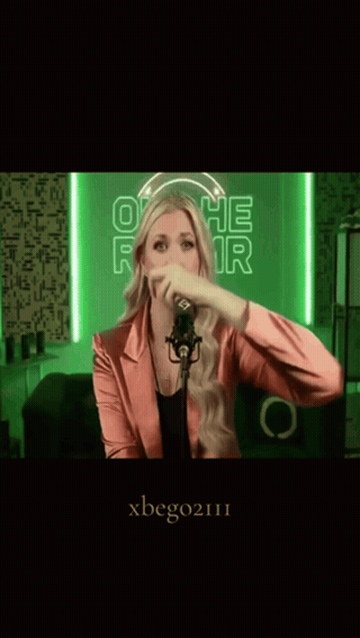A Woman In A Pink Jacket Is Singing Into A Microphone With Xbego2111 Written On The Bottom GIF