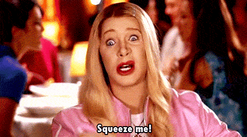A Woman In A Pink Jacket Is Sitting At A Table And Saying `` Squeeze Me ! '' GIF