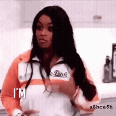 A Woman In A Pink Jacket Is Standing In A Kitchen Holding A Cup Of Coffee . GIF