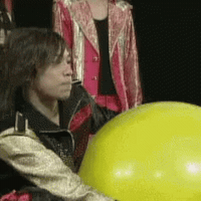 A Woman In A Pink Jacket Is Standing Next To A Yellow Balloon GIF