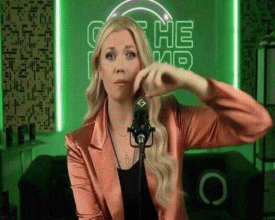 A Woman In A Pink Jacket Stands In Front Of A Microphone In Front Of A Green Sign That Says ' The ' GIF