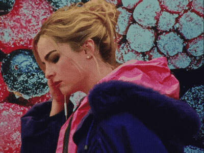 A Woman In A Pink Jacket With A Blue Fur Hood Looks Down GIF