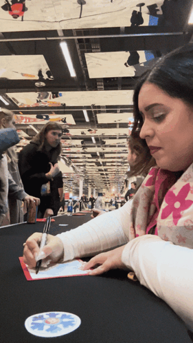 A Woman In A Pink Louis Vuitton Scarf Is Signing A Piece Of Paper GIF