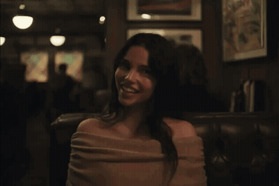 A Woman In A Pink Off The Shoulder Top Is Smiling In A Dark Room GIF
