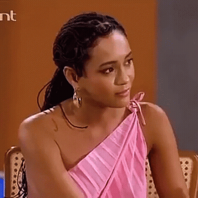 A Woman In A Pink One Shoulder Dress Is Sitting In A Chair And Looking At The Camera . GIF