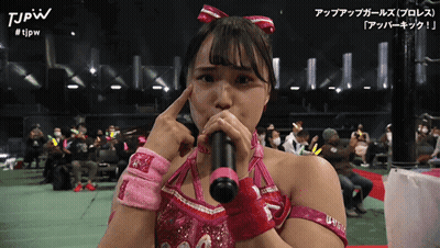 A Woman In A Pink Outfit Is Holding A Microphone And The Words Tjpw Are On The Bottom Right GIF