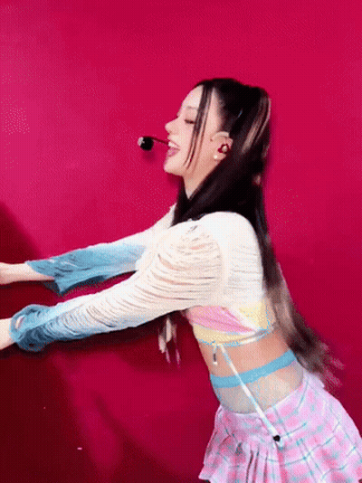 A Woman In A Pink Plaid Skirt Is Dancing In Front Of A Red Background GIF