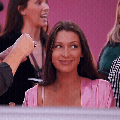 A Woman In A Pink Robe Is Smiling While Sitting In A Crowd Of People . GIF
