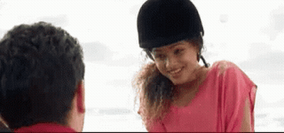 A Woman In A Pink Shirt And A Black Helmet Is Smiling At A Man . GIF