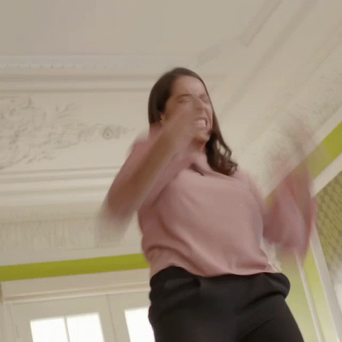 A Woman In A Pink Shirt And Black Pants Is Making A Funny Face GIF