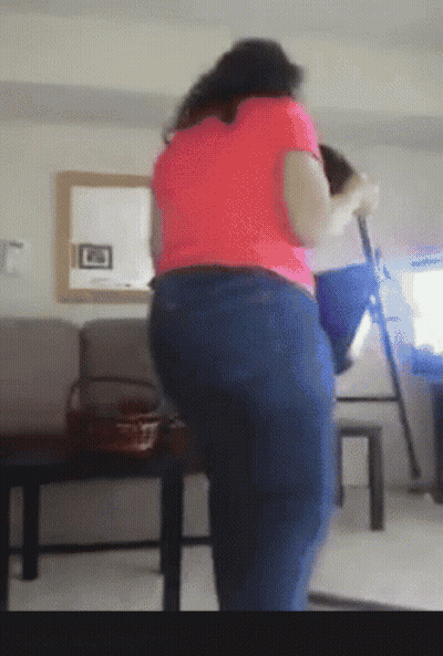 A Woman In A Pink Shirt And Blue Jeans Is Standing In Front Of A Mirror GIF