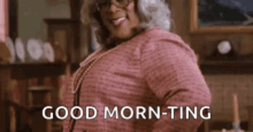 A Woman In A Pink Shirt And Glasses Is Standing In A Living Room And Saying `` Good Morning - Ting '' . GIF