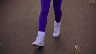 A Woman In A Pink Shirt And Purple Pants Is Jogging Down A Street . GIF