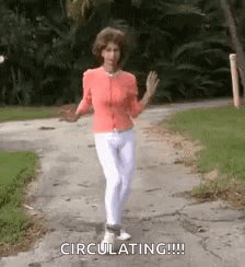 A Woman In A Pink Shirt And White Pants Is Dancing On A Sidewalk . GIF