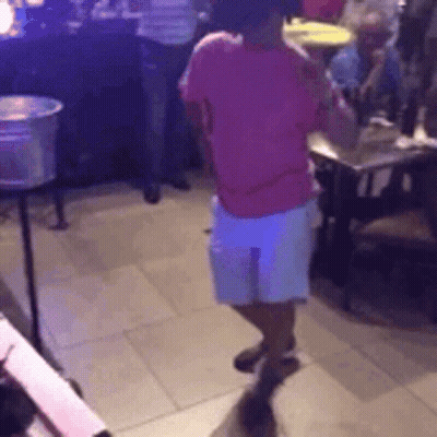 A Woman In A Pink Shirt And White Shorts Is Dancing In A Room With People . GIF