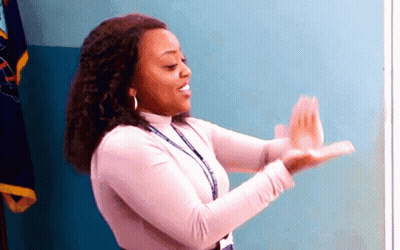 A Woman In A Pink Shirt Is Clapping Her Hands In Front Of A Flag . GIF