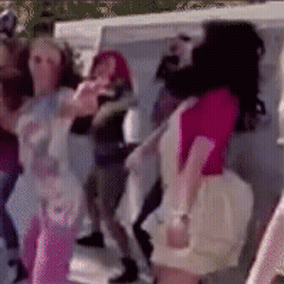 A Woman In A Pink Shirt Is Dancing In A Crowd Of People GIF