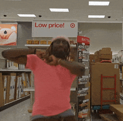 A Woman In A Pink Shirt Is Dancing In Front Of A Sign That Says Low Price GIF