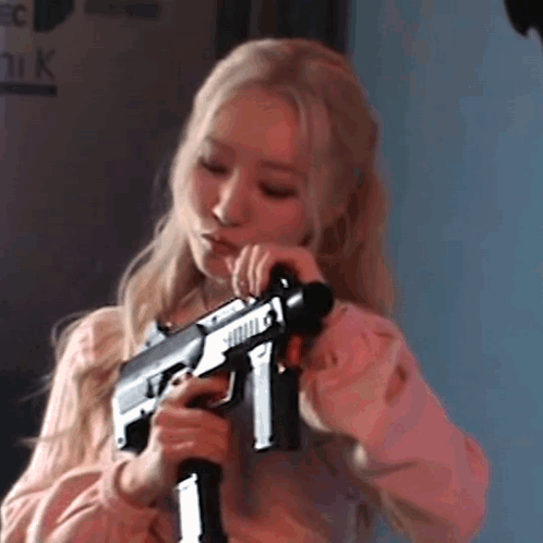 A Woman In A Pink Shirt Is Holding A Gun . GIF
