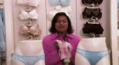A Woman In A Pink Shirt Is Holding A Pair Of Blue Underwear In Front Of Mannequins . GIF