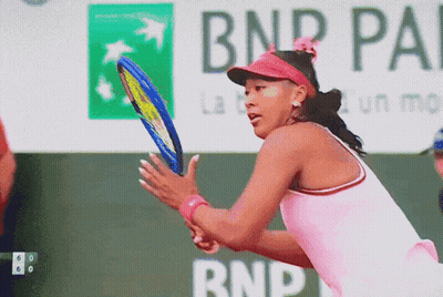 A Woman In A Pink Shirt Is Holding A Tennis Racquet In Front Of A Bnp Pa Sign GIF