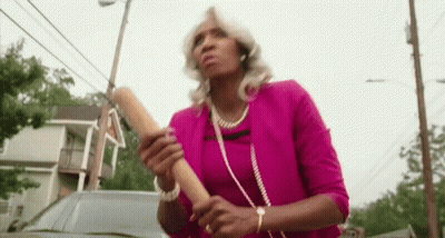 A Woman In A Pink Shirt Is Holding A Wooden Rolling Pin In Her Hands . GIF