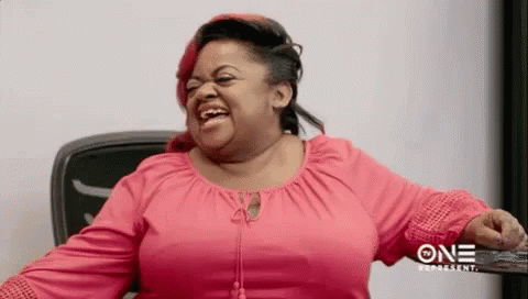 A Woman In A Pink Shirt Is Laughing While Sitting At A Table . GIF
