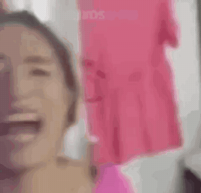 A Woman In A Pink Shirt Is Looking At The Camera . GIF