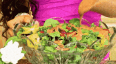 A Woman In A Pink Shirt Is Pouring Dressing On A Salad GIF