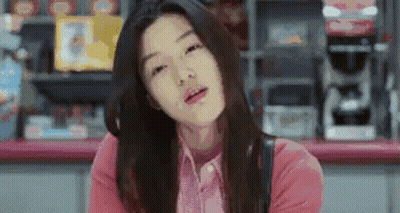 A Woman In A Pink Shirt Is Sitting At A Counter In A Store And Making A Funny Face . GIF