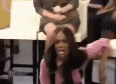 A Woman In A Pink Shirt Is Sitting On A Chair With Her Hand On Her Head . GIF