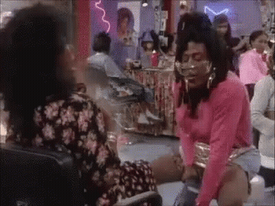 A Woman In A Pink Shirt Is Sitting On The Floor In A Room With A Group Of People . GIF