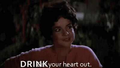 A Woman In A Pink Shirt Is Smiling And Says `` Drink Your Heart Out . '' GIF