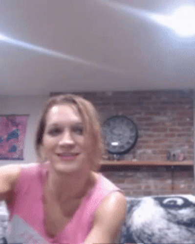 A Woman In A Pink Shirt Is Smiling In Front Of A Brick Wall And A Clock GIF