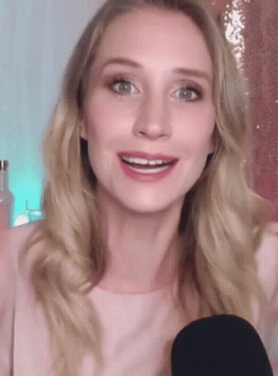A Woman In A Pink Shirt Is Smiling While Holding A Black Microphone GIF
