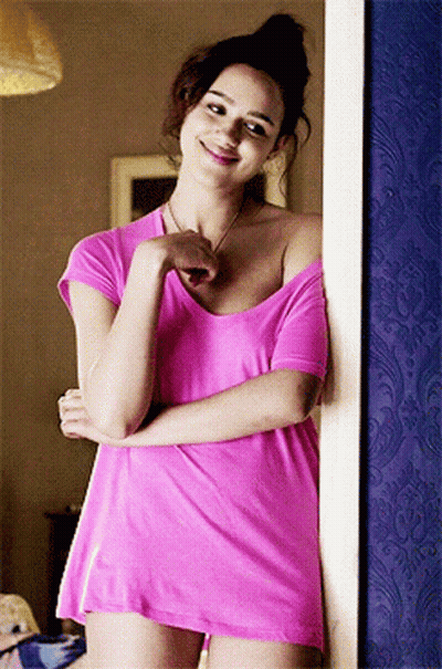 A Woman In A Pink Shirt Is Standing In Front Of A Blue Wall GIF
