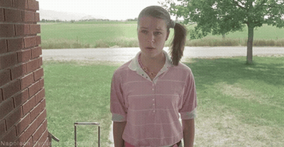 A Woman In A Pink Shirt Is Standing In Front Of A Brick Building GIF