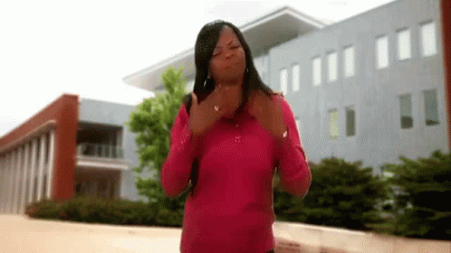 A Woman In A Pink Shirt Is Standing In Front Of A Building And Giving The Middle Finger . GIF