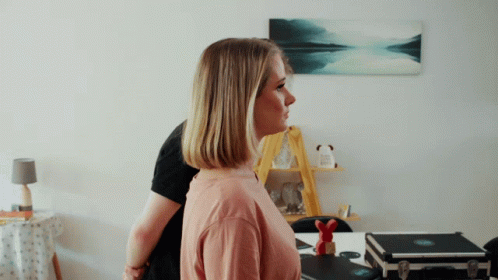 A Woman In A Pink Shirt Is Standing In Front Of A Man In A Black Shirt GIF